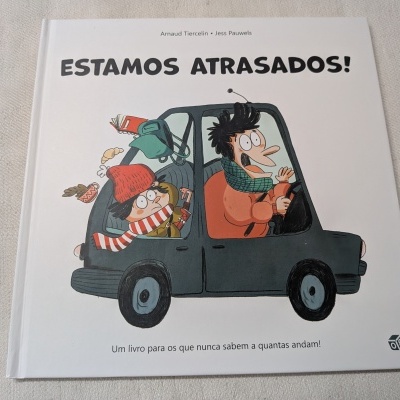 Capa de livro infantil com ilustração de duas pessoas dentro de um carro e título ESTAMOS ATRASADOS!