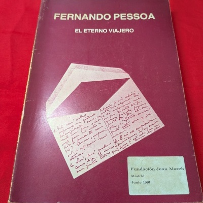 Livro roxo com título branco e envelope desenhado, sobre tecido vermelho.