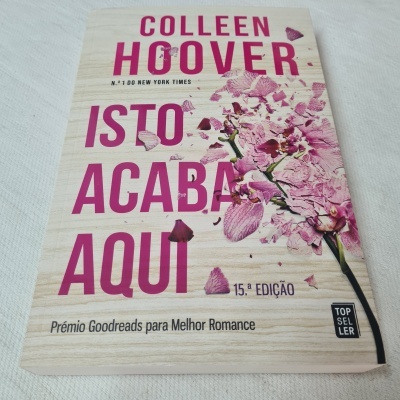 Capa do livro 'ISTO ACABA AQUI' de Colleen Hoover com flores rosas e fundo em textura de madeira clara