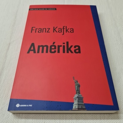 Livro 'Amérika' de Franz Kafka com capa vermelha e azul e Estátua da Liberdade