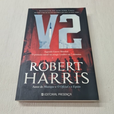 Livro capa mole V2 de Robert Harris com fundo preto e detalhes em cinza, vermelho e branco