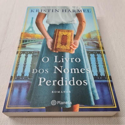 Capa do livro o Livro dos Nomes Perdidos com ilustração de mulher segurando livro antigo e Torre Eiffel ao fundo