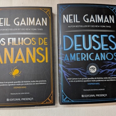 Dois livros em capa dura de Neil Gaiman, um amarelo e outro azul, sobre tecido claro.