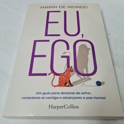 Capa do livro 'EU, EGO' com texto lilás, gato laranja e bola azul