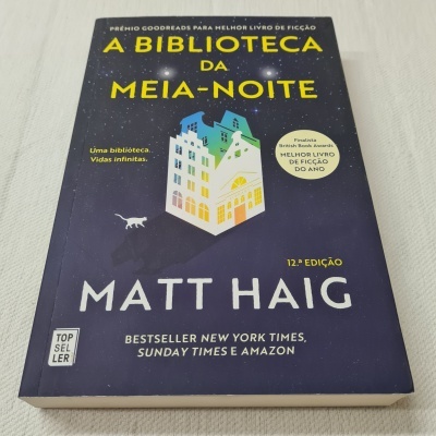 Capa do livro A Biblioteca da Meia-Noite de Matt Haig, fundo azul-escuro com ilustração de edifício colorido e texto em amarelo e branco.