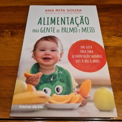 Capa de livro sobre alimentação infantil com bebé a segurar fruta e texto explicativo.