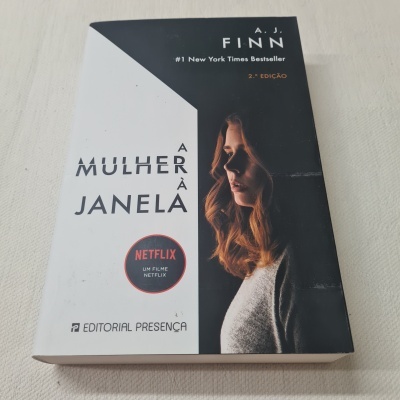 Capa do livro 'A Mulher à Janela' com imagem de mulher loira e selo Netflix.