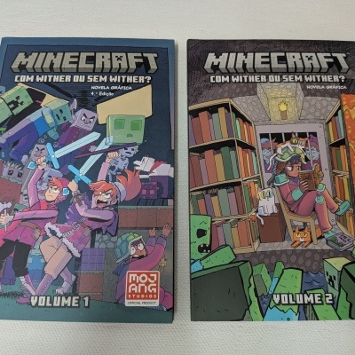 Dois livros de banda desenhada Minecraft volumes 1 e 2 sobre superfície clara.