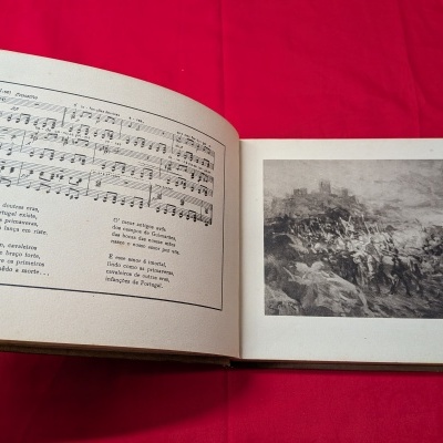 Livro aberto com partitura musical e texto em português de um lado e imagem em preto e branco de uma batalha do outro.