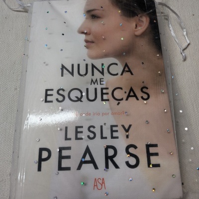 Capa de livro com título NUNCA ME ESQUEÇAS de Lesley Pearse dentro de saco transparente com pontos brilhantes prateados