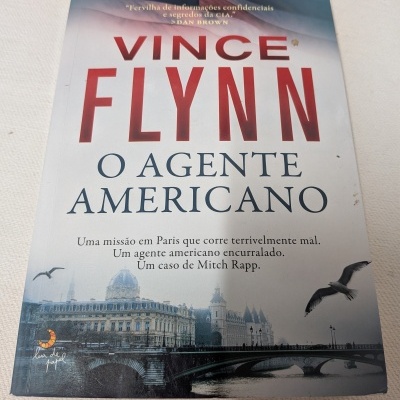 Capa do livro O Agente Americano de Vince Flynn com ilustração de uma cidade e pássaros