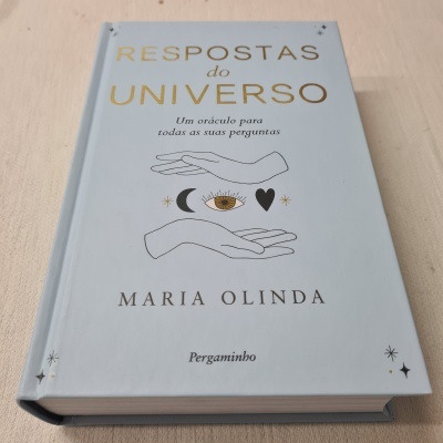 Livro azul-claro intitulado Respostas do Universo com ilustrações de mãos, olho, lua e coração