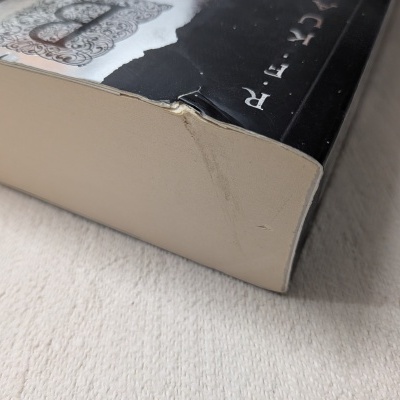 Livro com capa preta e branca com canto danificado sobre superfície clara