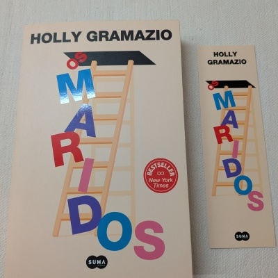 Livro 'Os Maridos' com capa branca e ilustração de escada colorida ao lado de marcador de livros