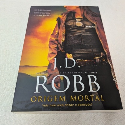 Capa do livro Origem Mortal de J.D. Robb com pessoa vestindo colete policial preto e casaco castanho