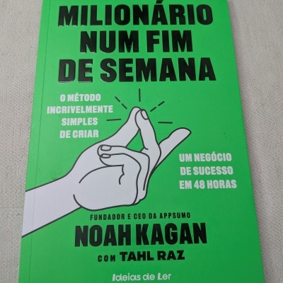 Livro verde com título Milionário num fim de semana e ilustração de mão, sobre superfície cinzenta.