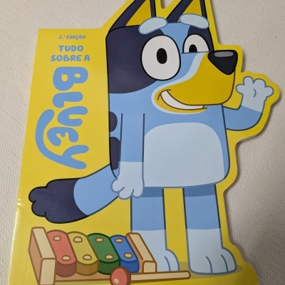 Livro infantil Bluey com capa dura em forma de cão azul cartoon e fundo amarelo