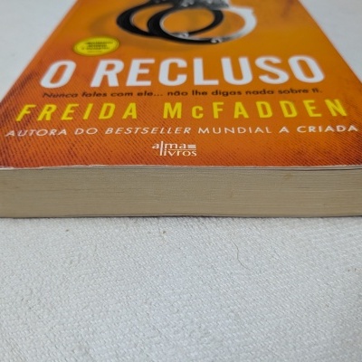 Capa de livro laranja com título O RECLUSO e autoria de FREIDA McFADDEN