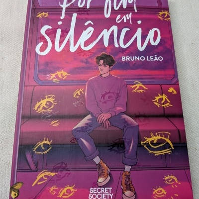 Capa de livro Por fim em silêncio com ilustração de jovem sentado e olhos amarelos desenhados
