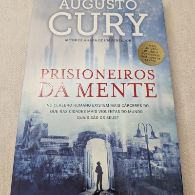 Capa do livro Prisioneiros da Mente de Augusto Cury com fundo de cidade e silhueta de pessoa.