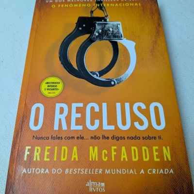 Capa do livro O Recluse com fundo laranja e imagem de algemas pretas