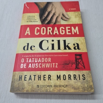 Capa de livro com texto 'A CORAGEM de Cilka O TATUADOR DE AUSCHWITZ' e imagem de mão sobre fundo texturizado