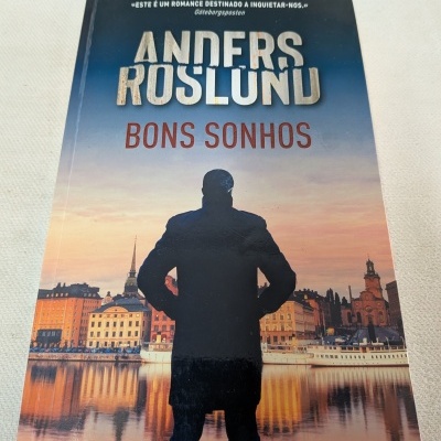 Livro Bons Sonhos de Anders Roslund com capa com silhueta de homem e cidade ao pôr do sol
