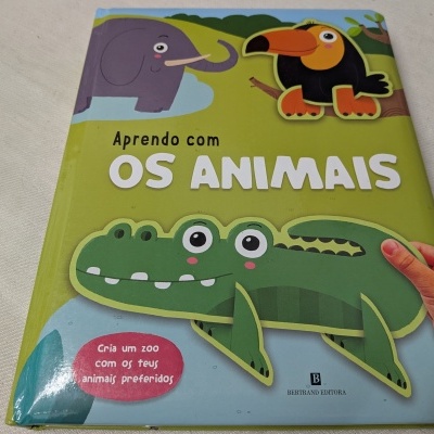 Capa de livro infantil Aprendo com OS ANIMAIS com ilustrações de animais e mão à direita.