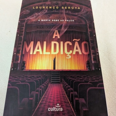 Livro A Maldição com capa de auditório teatral e cortina amarela.