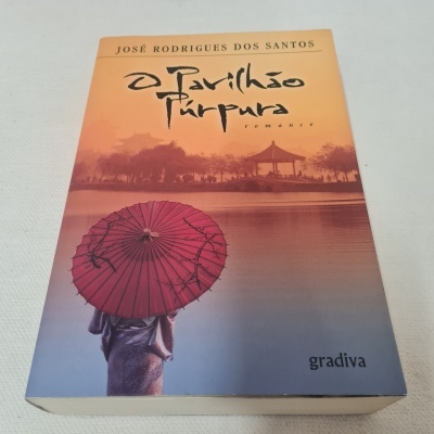 Capa do livro 'O Gavilhão Púrpura' com pessoa e guarda-chuva vermelho diante de paisagem junto a um lago