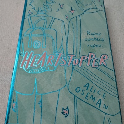 Livro Heartstopper Volume 1 com capa verde-azulada ilustrada e texto em azul e rosa metálico
