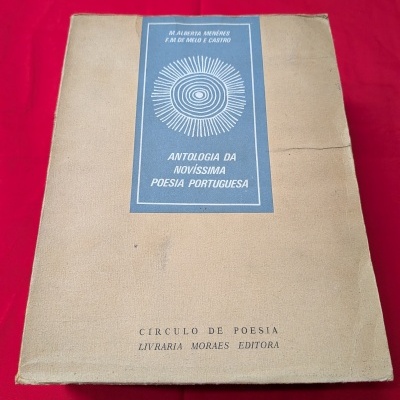 Capa de livro com etiqueta azul e texto em branco, sobre tecido vermelho.