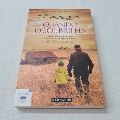 Capa de livro 'Quando O Sol Brilha' com homem e criança num campo