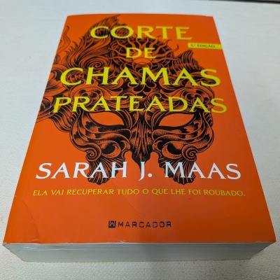 Livro 'Corte de Chamas Prateadas' com capa laranja e máscara preta