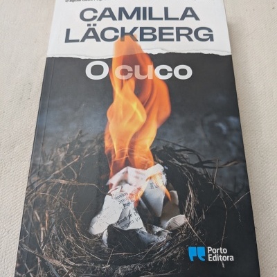 Capa do livro O Cuco com ninho e papéis em chamas