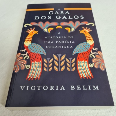 Capa do livro 'A Casa dos Galos' com galos coloridos em fundo azul