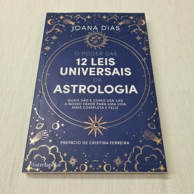Livro azul escuro com texto dourado sobre 12 leis universais da astrologia
