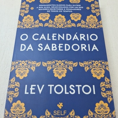 Livro azul com padrões florais amarelos e texto 'O CALENDÁRIO DA SABEDORIA'