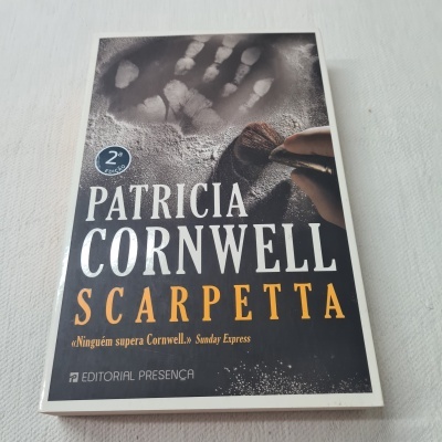 Livro 'Scarpetta' de Patricia Cornwell com capa preta, letras amarelas e branca, e imagem de mão em pó branco.
