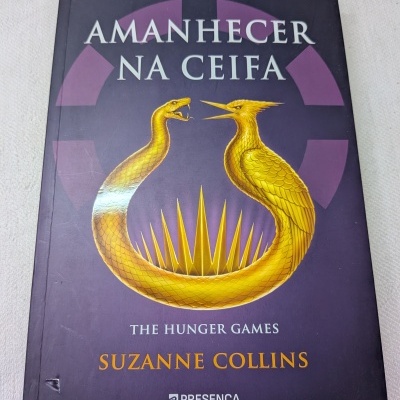 Capa de livro Amanhecer na Ceifa de Suzanne Collins com ilustração dourada de serpente e pássaro