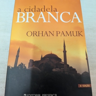 Capa do livro a cidadela BRANCA de Orhan Pamuk, tons de laranja e preto, texto e selo editorial.