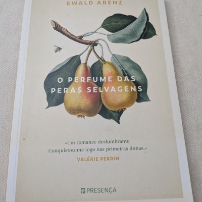 Livro O Perfume das Peras Selvagens com ilustração e texto na capa sobre tecido claro.