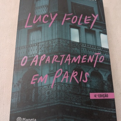 Capa do livro O APARTAMENTO EM PARIS de Lucy Foley com fundo de edifício e detalhes em rosa.