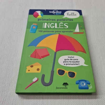 Livro infantil verde com imagens coloridas e texto em português sobre primeiras palavras em inglês