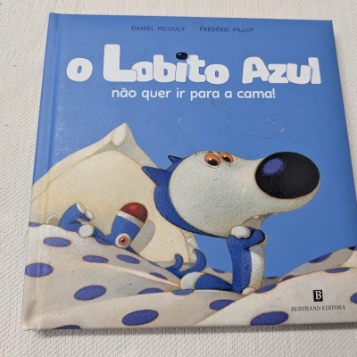 Capa de livro infantil azul com ilustração de cão azul e cobertor com bolinhas roxas