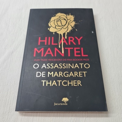 Capa de livro preto com texto em vermelho, branco e amarelo e uma rosa dourada no topo
