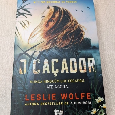 Livro O Caçador com capa mostrando mulher loira junto a um lago