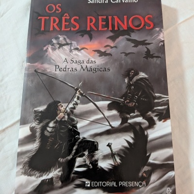 Capa do livro 'Os Três Reinos' de Sandra Carvalho com ilustração de duas figuras vestidas com pele em cenário nevado