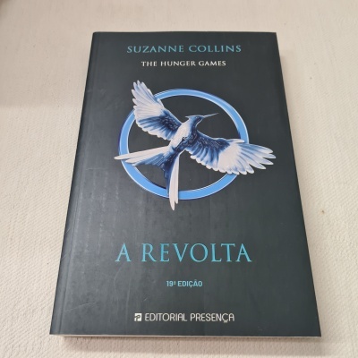 Livro A Revolta de Suzanne Collins com capa preta e pássaro azul e branco