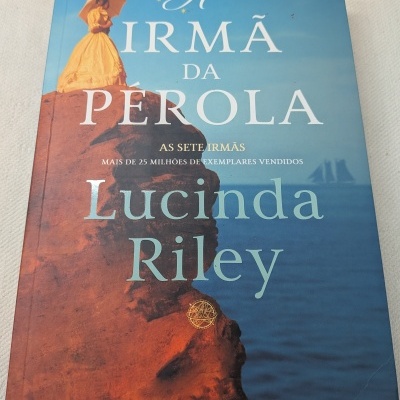 Capa de livro A Irmã da Pérola de Lucinda Riley com mulher de vestido amarelo em rocha